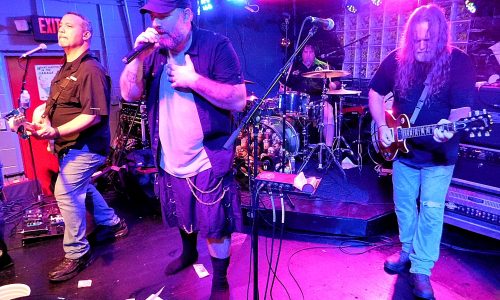 Rock band performs live onstage with singer at center.