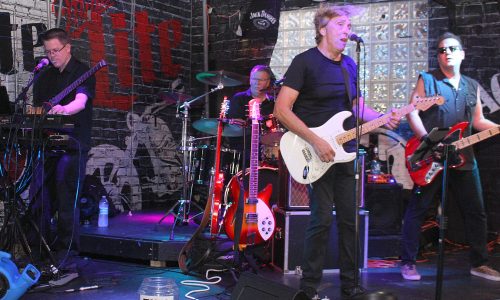 Band performs live onstage with singer-guitarist at center.