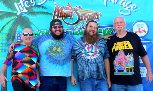 Four men pose smiling in front of a Main Street banner.