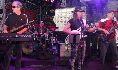 Band performs live onstage with guitarist singing at center