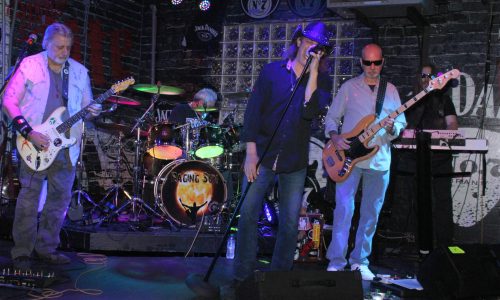 Band performs onstage with singer at center.