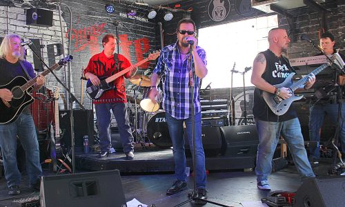 Band plays live onstage with singer at center.
